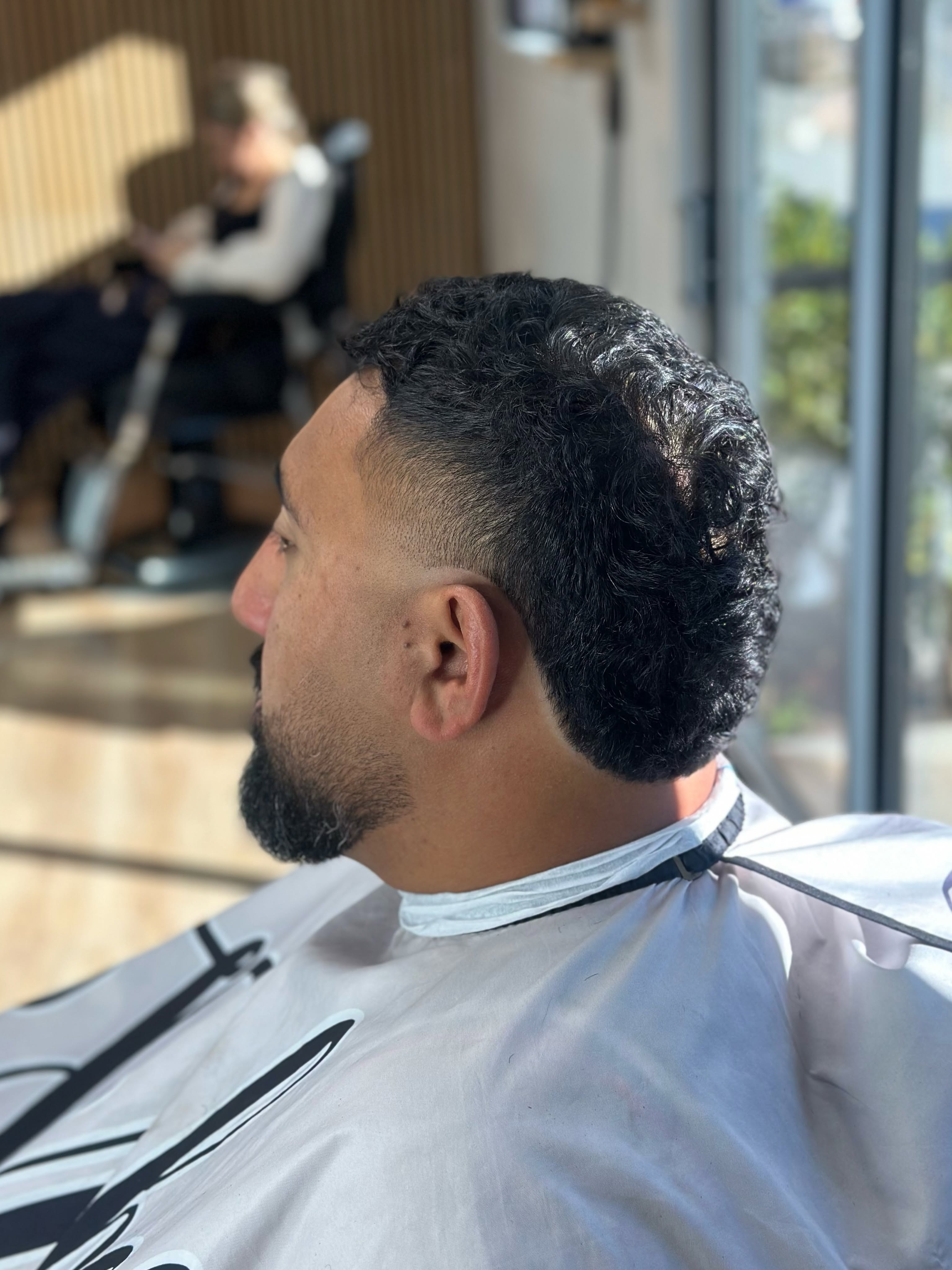 Side view of a curly top with a fade and a trimmed beard.